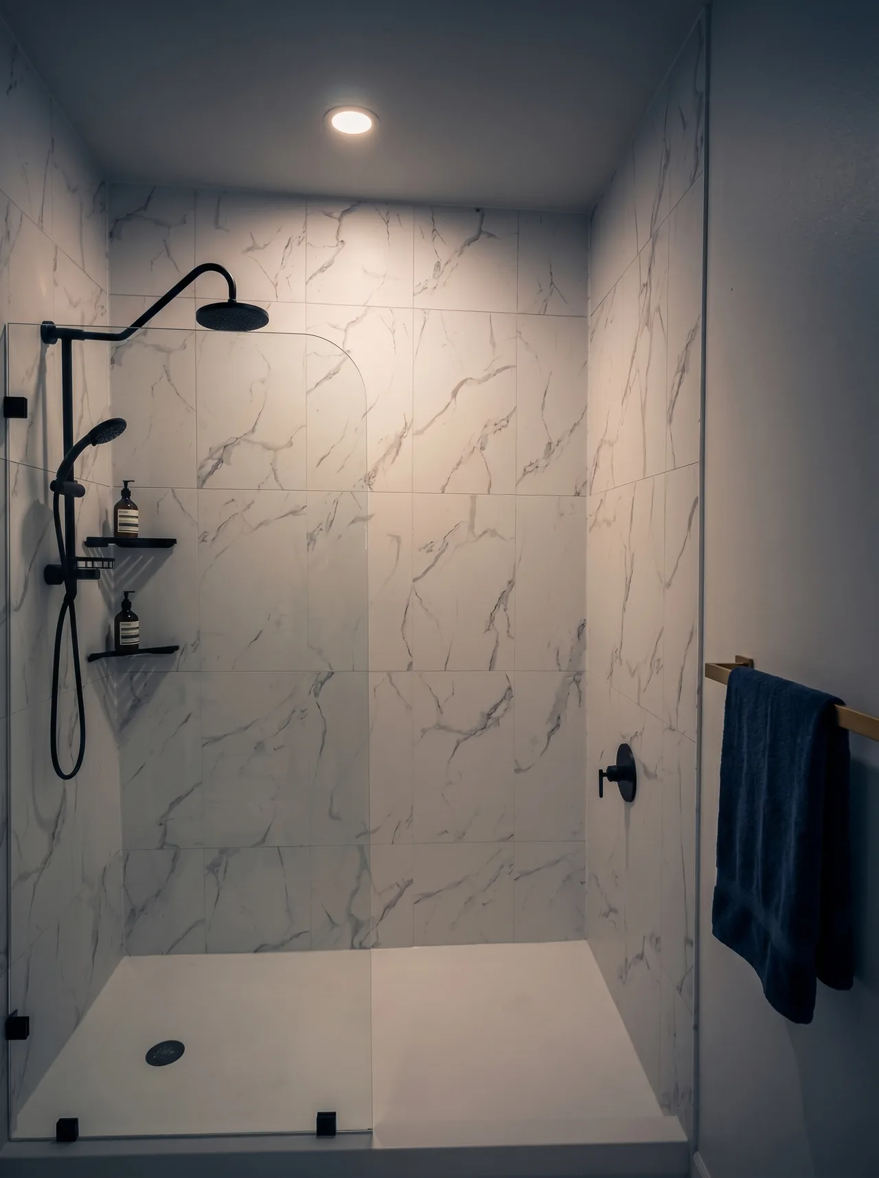Completed walk-in shower with white Carrara-look marble tile, matte black rain shower and fixtures, and a brushed brass towel bar